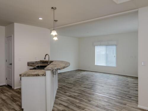 An empty living room with hardwood floors and a kitchen.